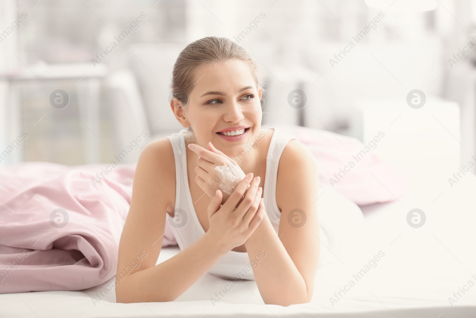 Photo of Young woman applying hand cream on bed at home