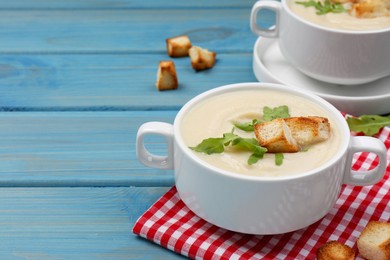 Bowls with tasty creamy soup of parsnip on light blue wooden table, space for text