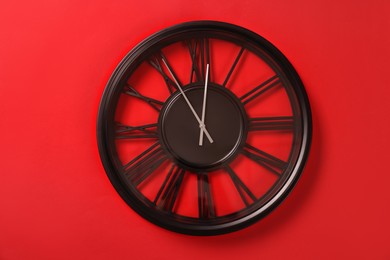 Photo of Clock showing five minutes until midnight on red background. New Year countdown