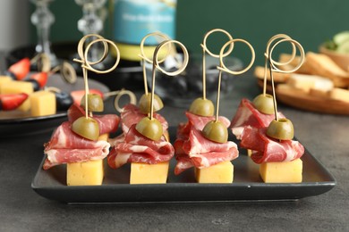 Photo of Tasty canapes with olives, prosciutto and cheese on grey table, closeup