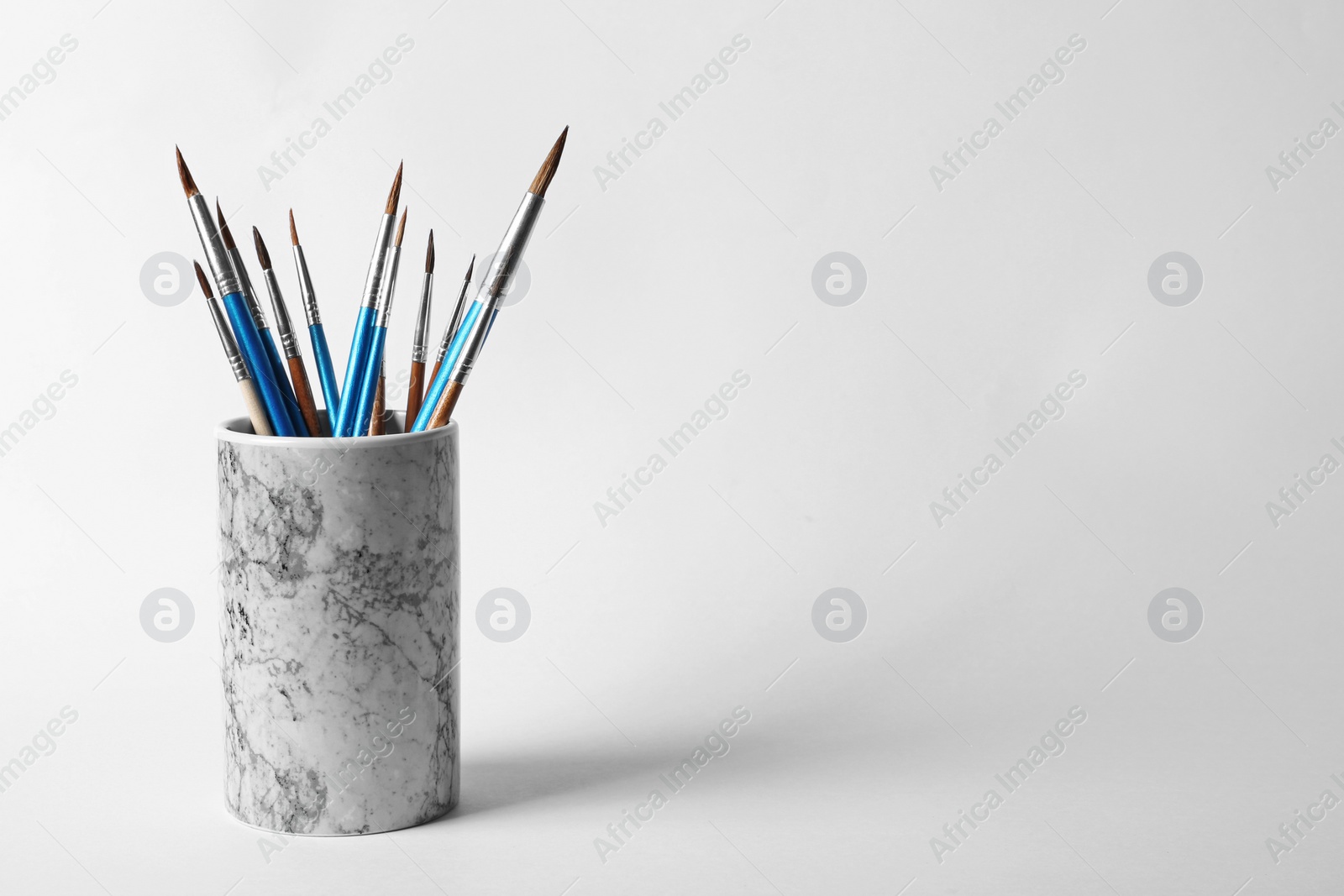 Photo of Holder with different paint brushes on white background. Space for text