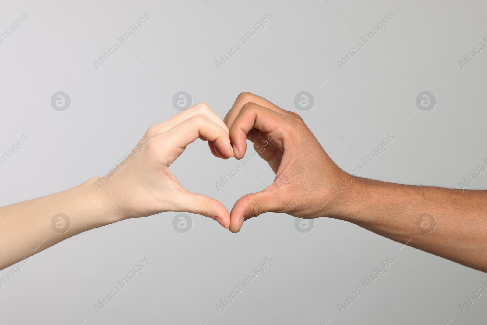 Photo of International relationships. People making heart with hands on light grey background, closeup