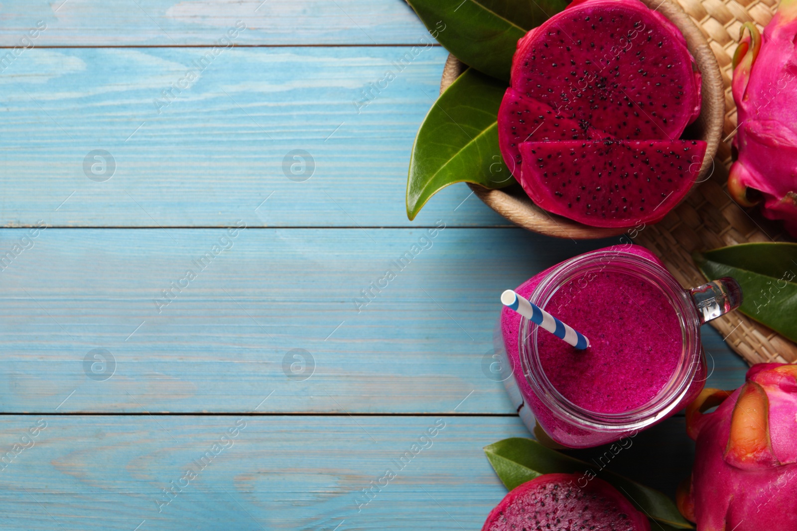 Photo of Delicious pitahaya smoothie in mason jar and fresh fruits on light blue wooden table, flat lay. Space for text