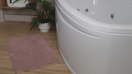 Photo of Soft bath mat near tub on wooden floor in bathroom