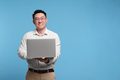 Photo of Happy man with laptop on light blue background, space for text