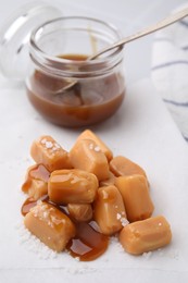 Yummy caramel candies and sea salt on white table