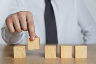 Photo of Businessman arranging blank cubes on wooden table, closeup. Space for text
