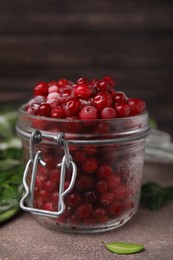Frozen red cranberries in glass jar on brown textured table, closeup