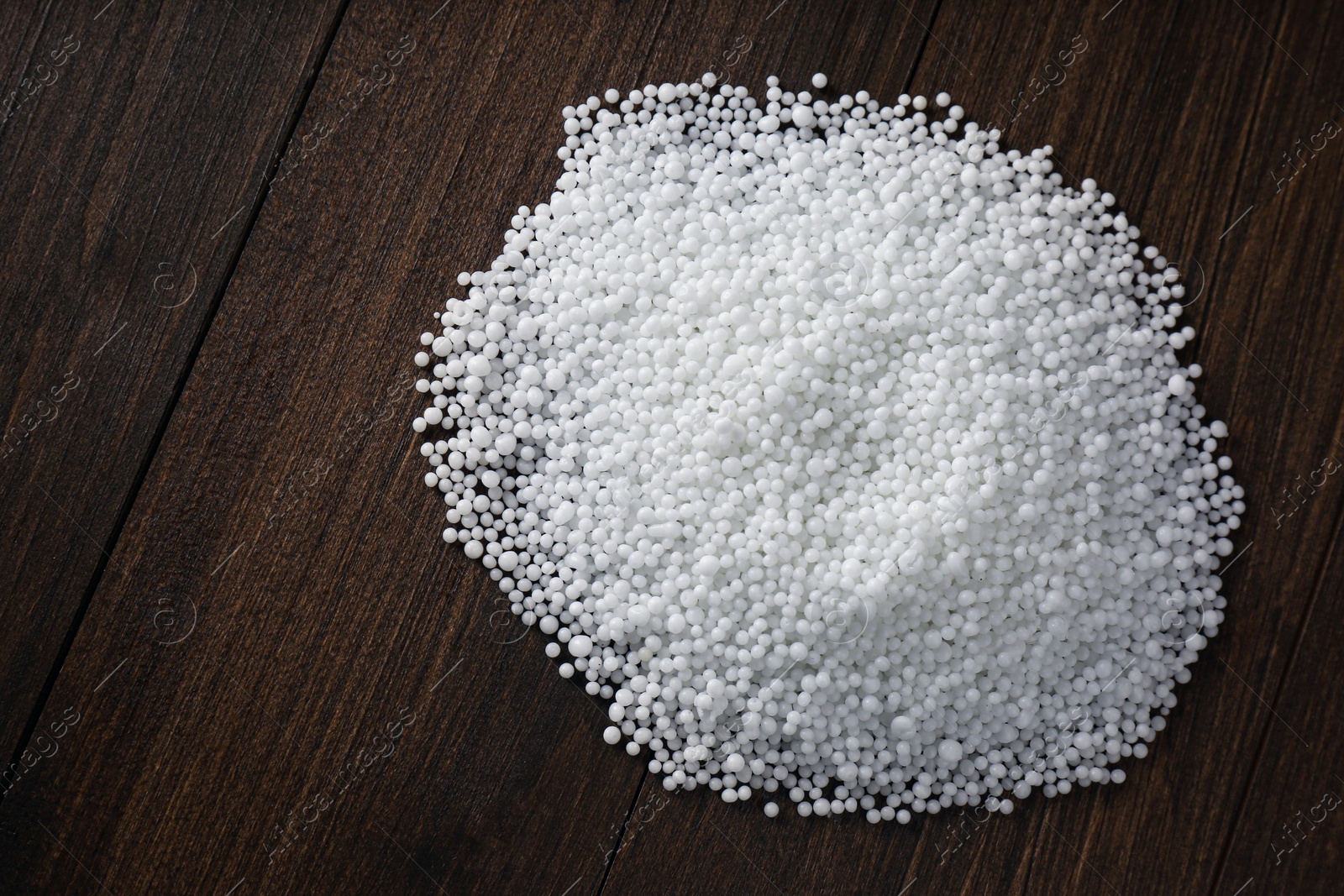 Photo of Pellets of ammonium nitrate on wooden table, flat lay with space for text. Mineral fertilizer