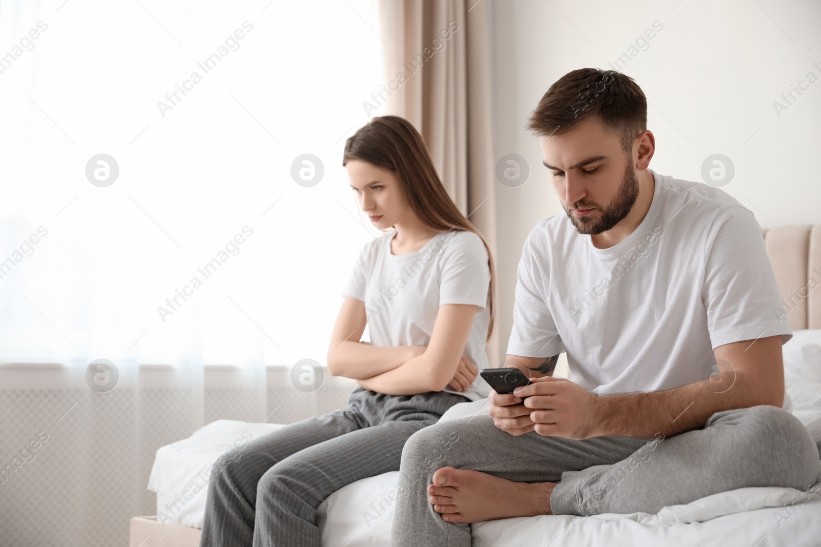 Photo of Man with smartphone ignoring his girlfriend at home. Relationship problems