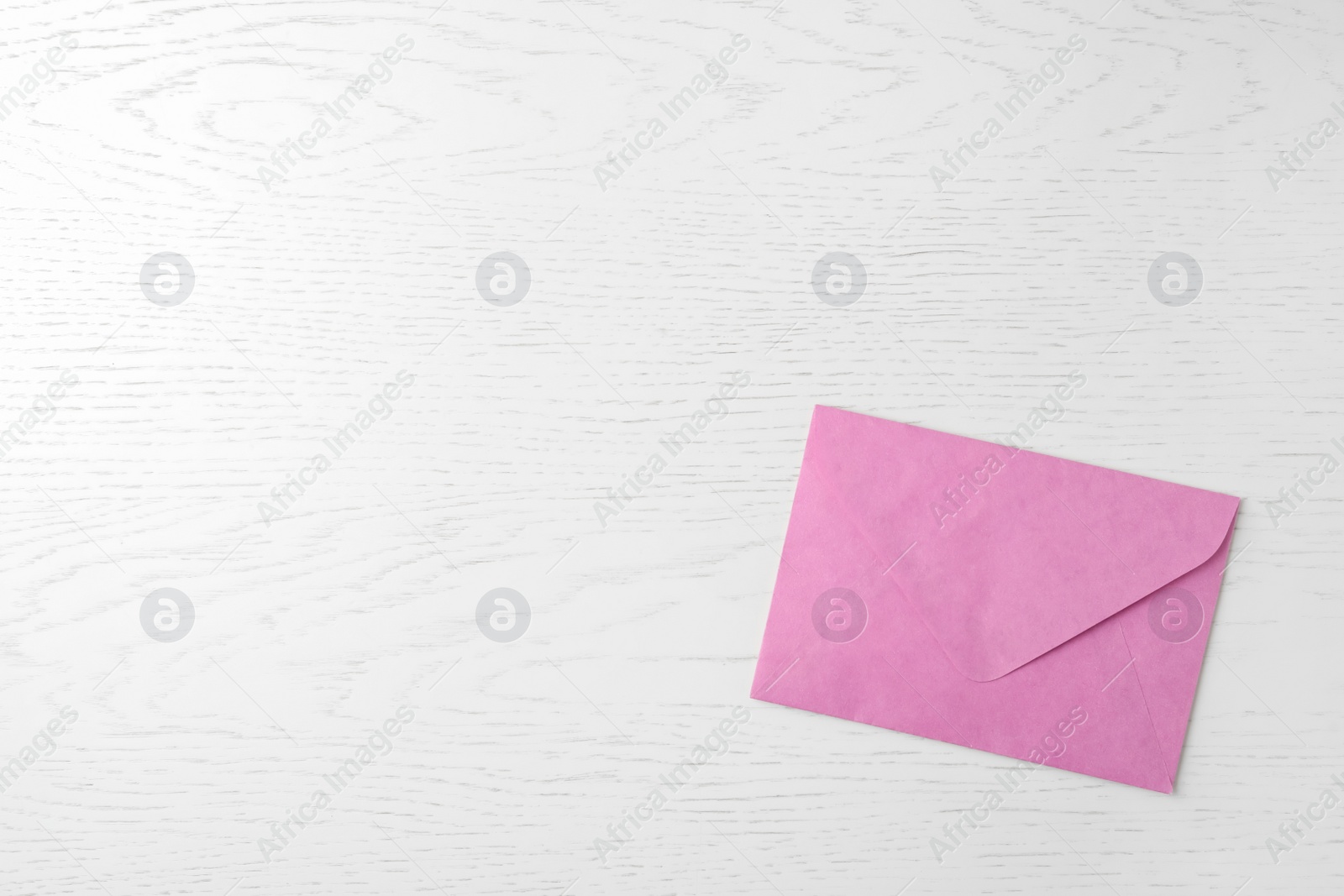 Photo of Pink paper envelope on white wooden background, top view. Space for text