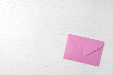 Pink paper envelope on white wooden background, top view. Space for text