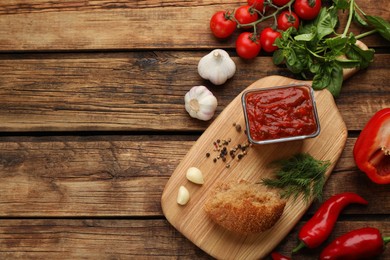 Delicious adjika sauce in bowl with bread and ingredients on wooden table, flat lay. Space for text