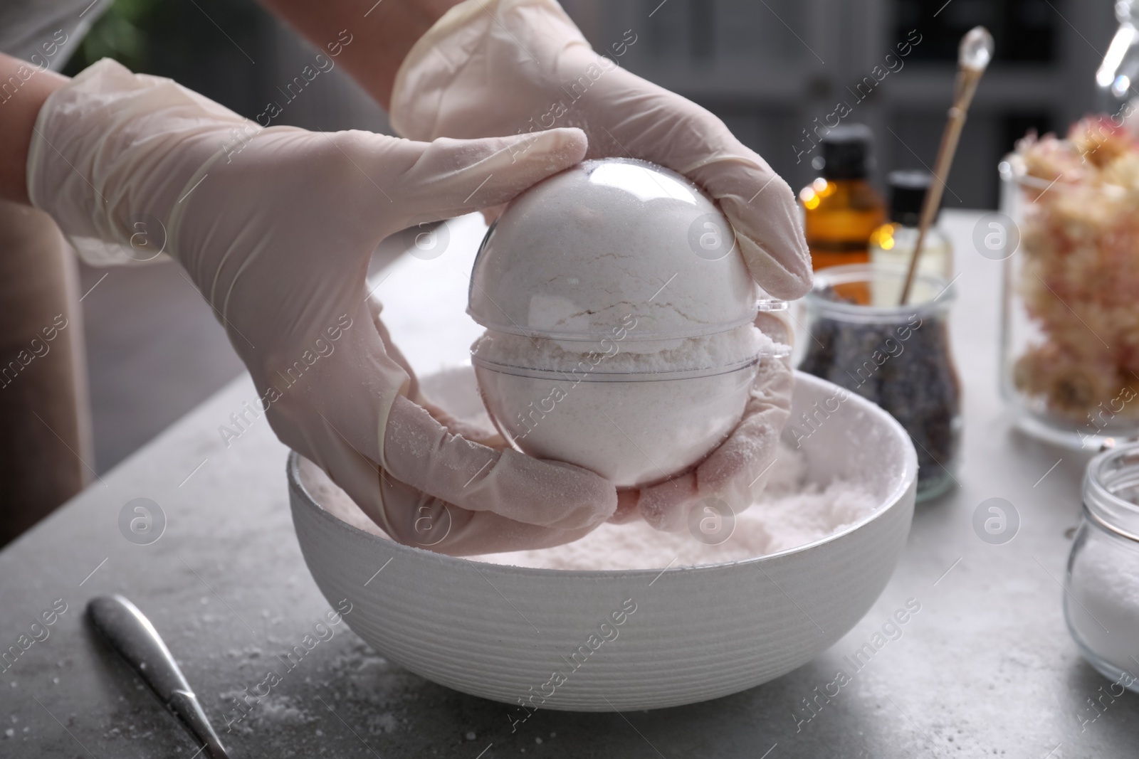 Photo of Woman in gloves making bath bomb at grey table, closeup