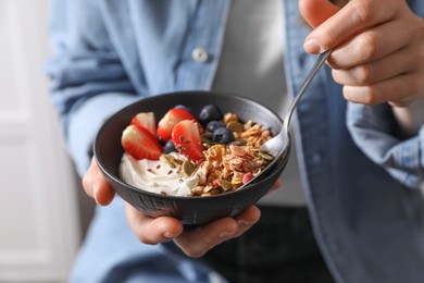 Photo of Woman eating tasty granola with berries, yogurt and seeds, closeup