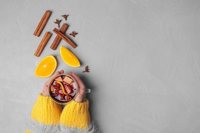 Woman holding cup of hot mulled wine on table, top view with space for text