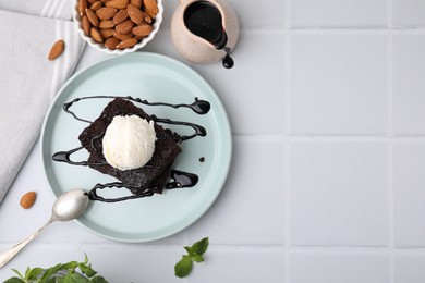 Tasty brownies served with ice cream and chocolate sauce on white tiled table, flat lay. Space for text