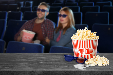 Image of Popcorn, 3D glasses, tickets on table and young couple in cinema hall, space for text 