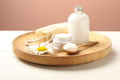 Photo of Cosmetic products, chamomile and loofah on white wooden table against pink background
