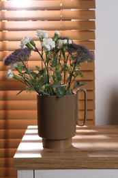Stylish ceramic vase with beautiful flowers and eucalyptus branches on wooden table near window