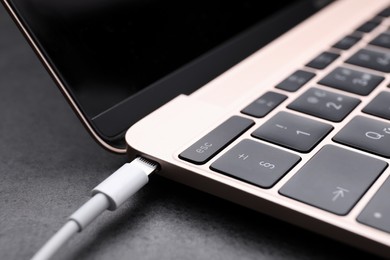 Photo of USB cable with lightning connector and laptop on black table, closeup