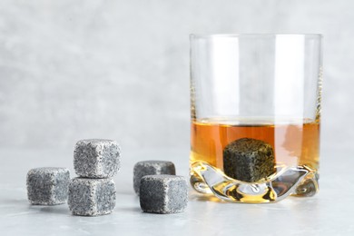 Whiskey stones and drink in glass on light marble table, closeup