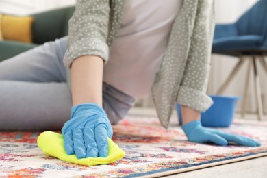 Photo of Woman in rubber gloves cleaning carpet with rag indoors, closeup. Space for text