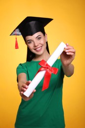 Photo of Happy student with graduation hat against yellow background, focus on diploma