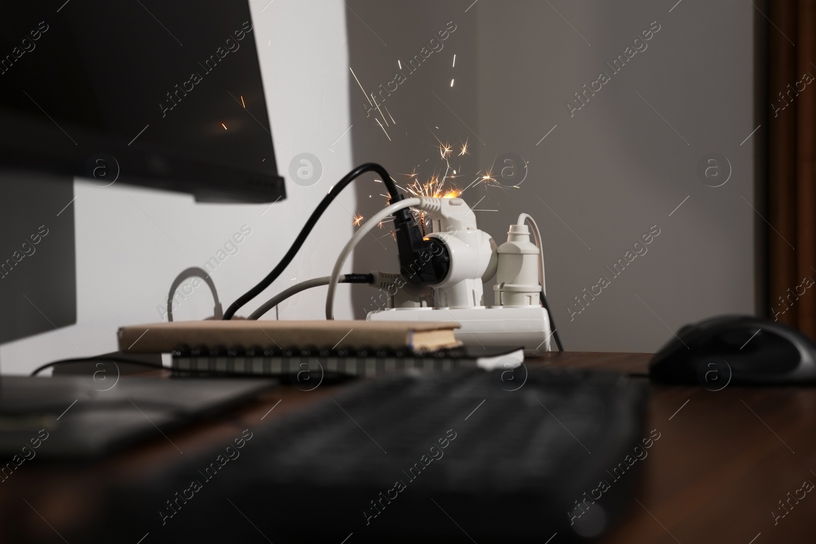 Photo of Inflamed plug in power strip indoors on wooden table. Electrical short circuit