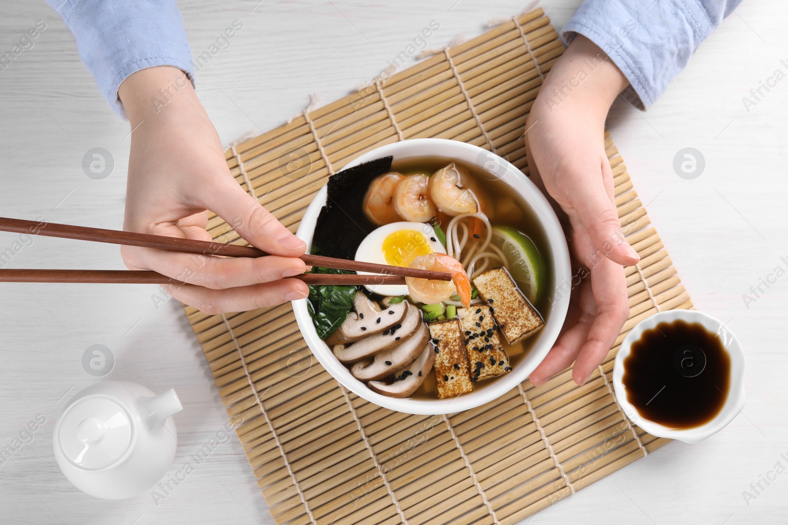 Photo of Woman eating delicious ramen with chopsticks at white table, top view. Noodle soup