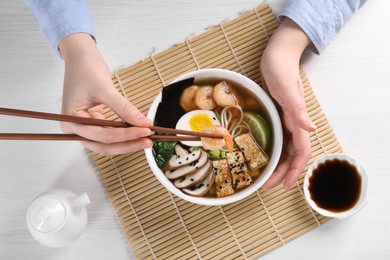 Photo of Woman eating delicious ramen with chopsticks at white table, top view. Noodle soup