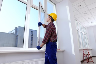 Photo of Worker in uniform installing plastic window indoors