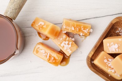 Yummy caramel candies, sauce and sea salt on white wooden table, top view