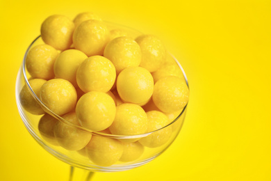 Photo of Tasty lemon chewing gums in glass on yellow background