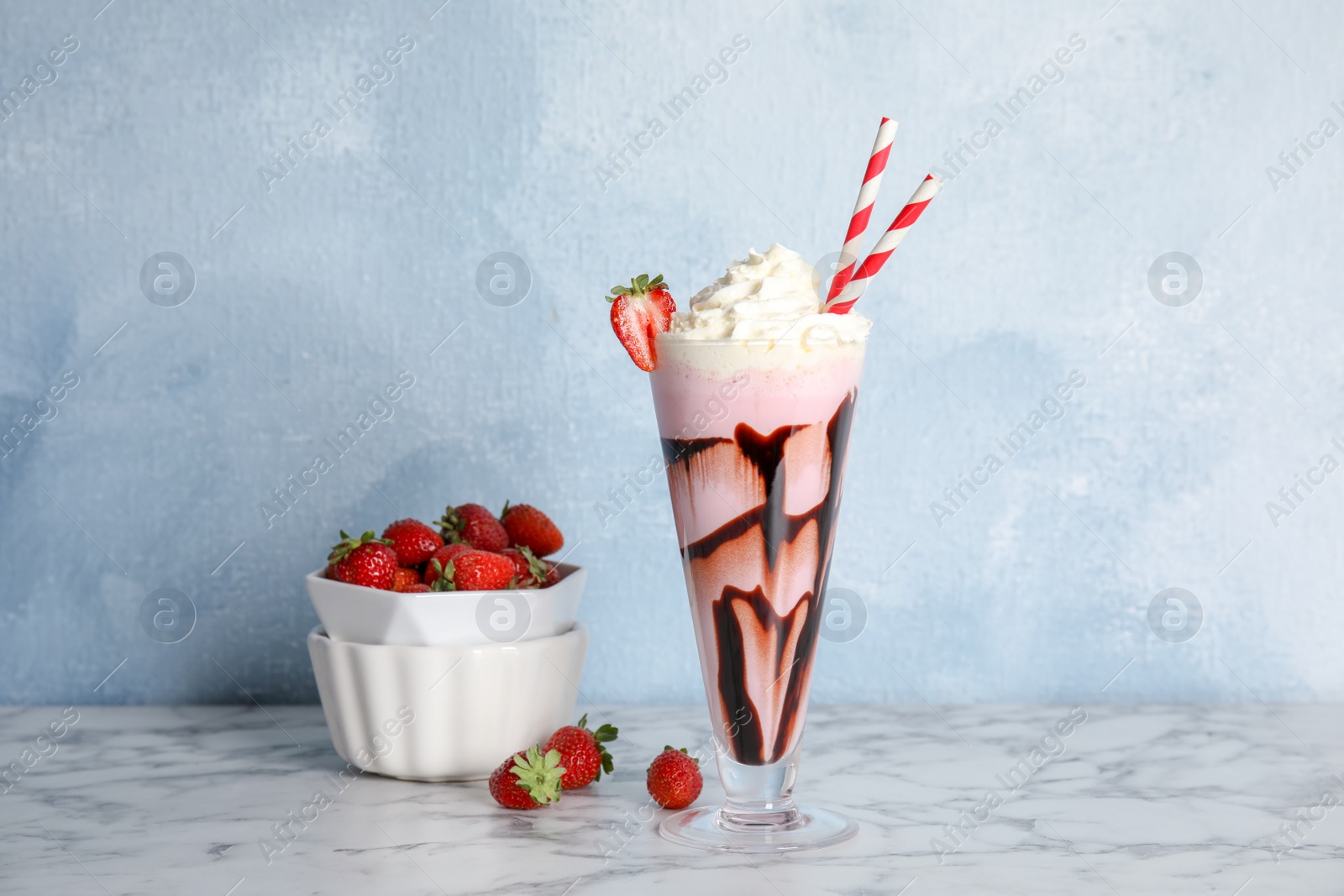 Photo of Glass of delicious milk shake and bowl with strawberries on table