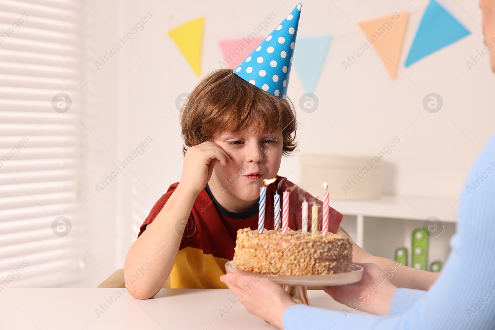 Photo of Birthday celebration. Mother holding tasty cake with burning candles near her son indoors