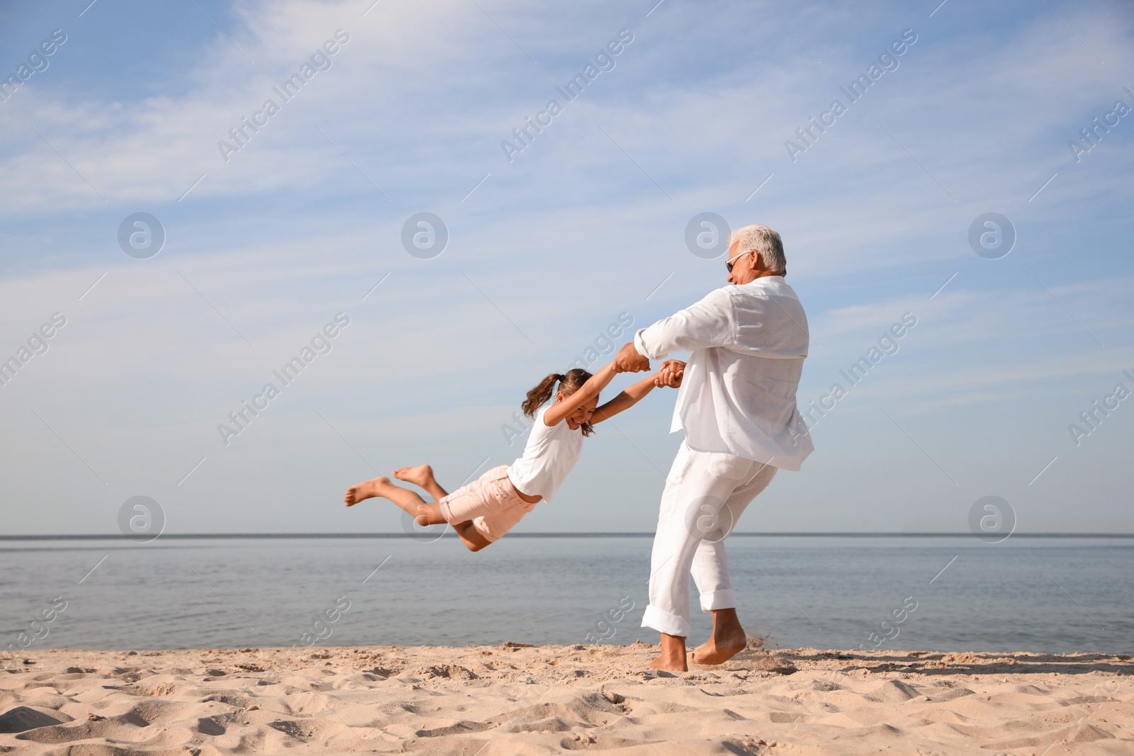 Photo of Cute little girl with grandfather spending time together on sea beach