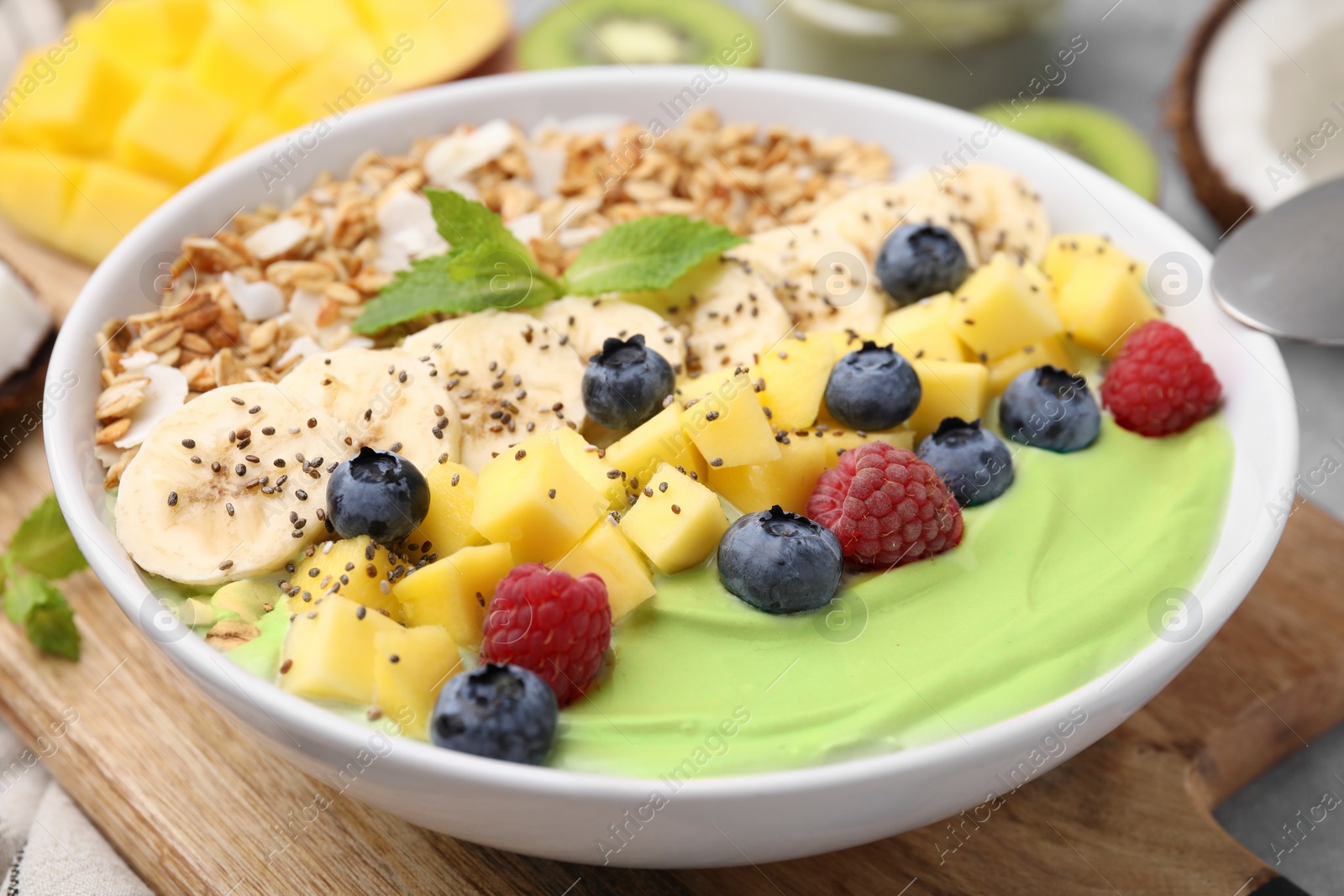 Photo of Tasty matcha smoothie bowl served with fresh fruits and oatmeal on table, closeup. Healthy breakfast