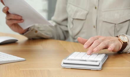 Professional accountant using calculator at wooden desk in office, closeup