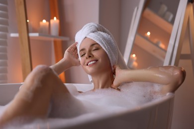 Photo of Beautiful woman taking bath in tub with foam indoors. Romantic atmosphere