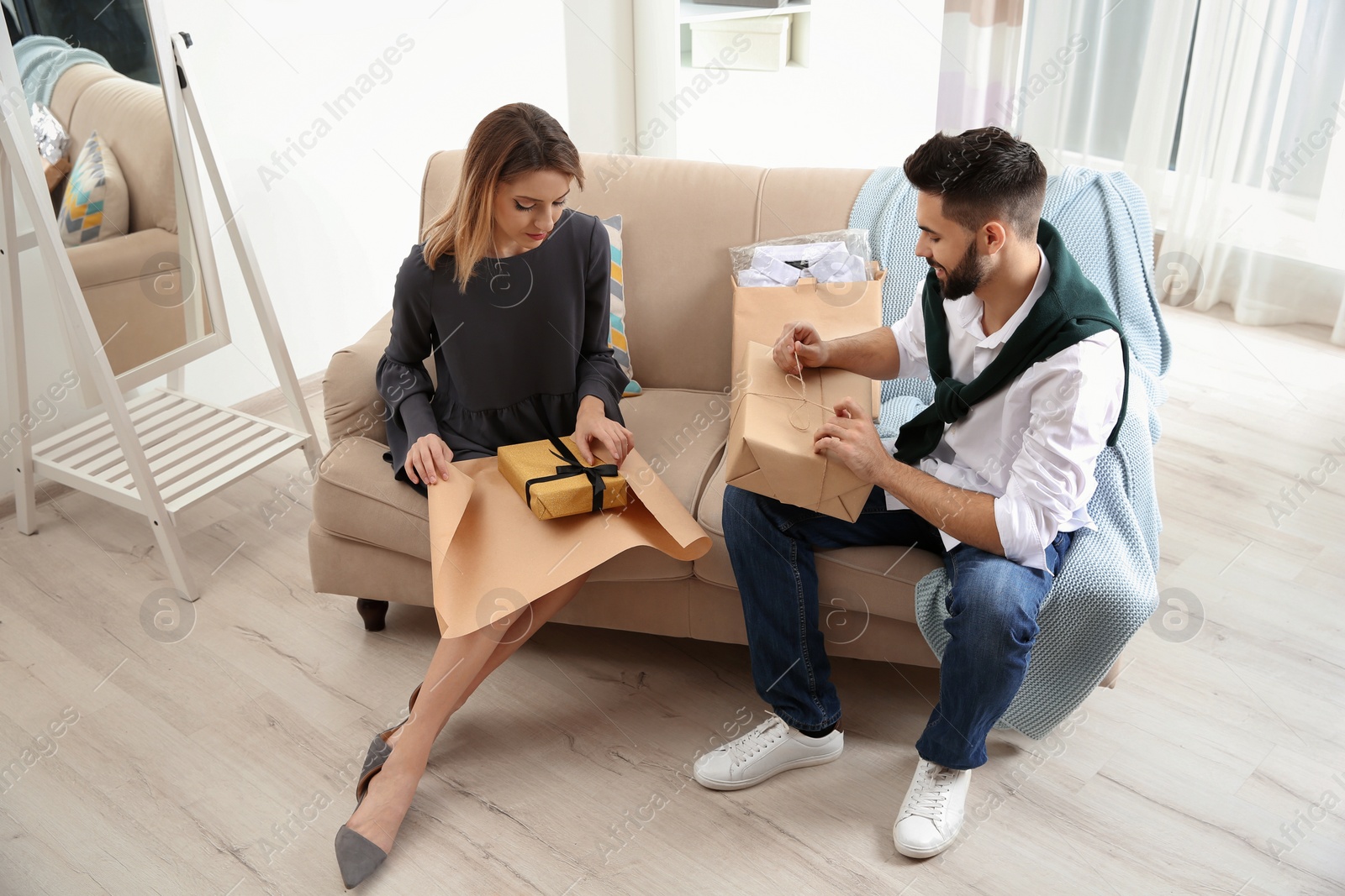 Photo of Young couple opening parcels on sofa in living room