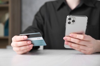 Online payment. Woman with smartphone and credit card at white wooden table, closeup