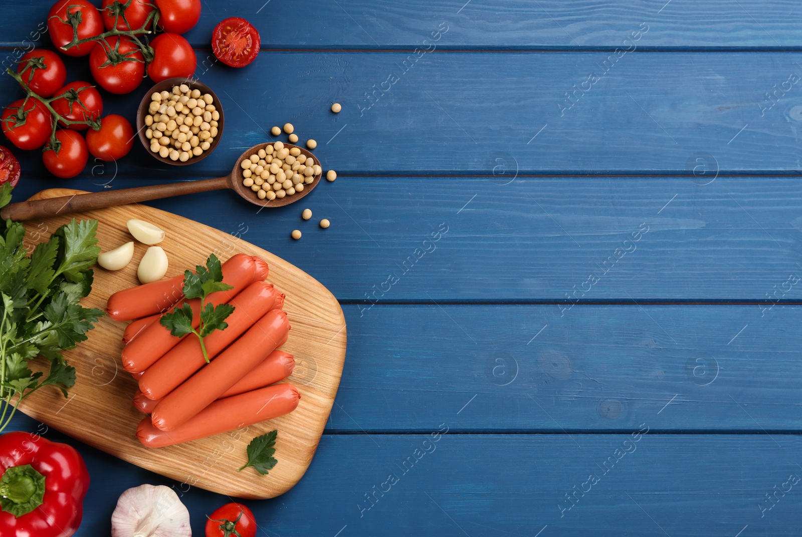 Photo of Fresh raw vegetarian sausages, soybeans and vegetables on blue wooden table, flat lay. Space for text