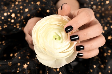 Photo of Woman with black manicure holding beautiful flower on dark background, closeup. Nail polish trends