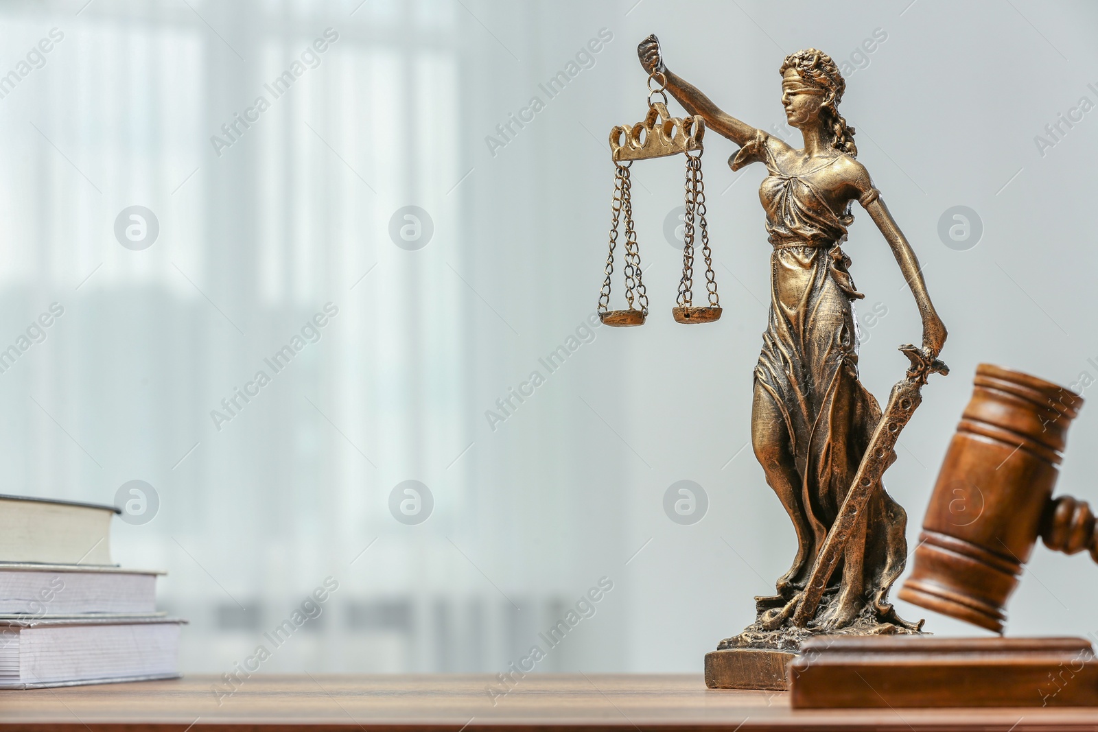 Photo of Figure of Lady Justice, gavel and books on table indoors, space for text. Symbol of fair treatment under law