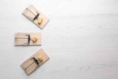 Mousetraps with pieces of cheese and space for text on white wooden background, flat lay. Pest control