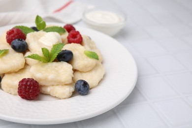 Plate of tasty lazy dumplings with berries, butter and mint leaves on white tiled table, closeup. Space for text