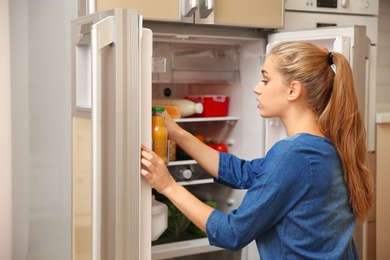 Photo of Young woman taking food from refrigerator at home