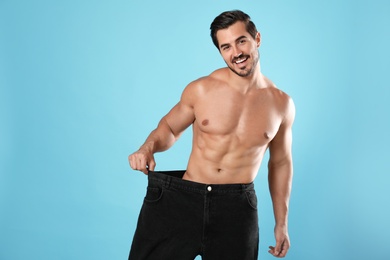 Young man with slim body in old big size jeans on light blue background