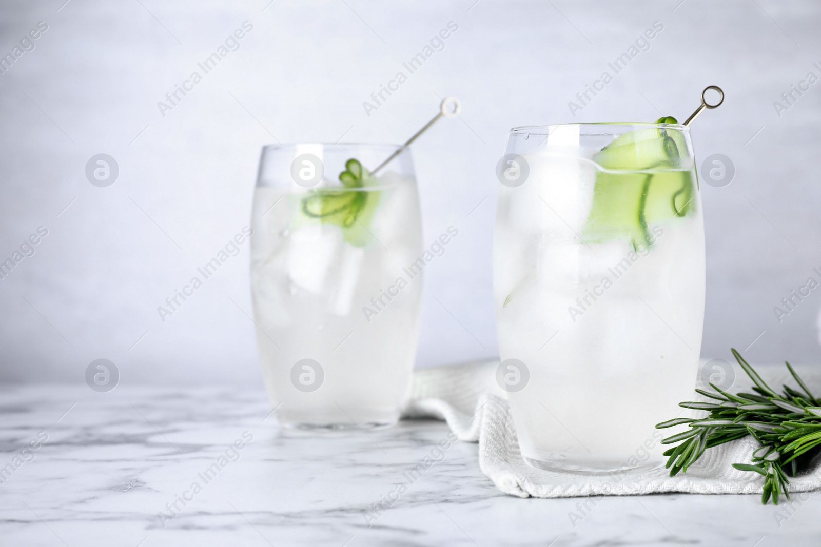 Photo of Glasses of martini with cucumber on marble table against light background. Space for text